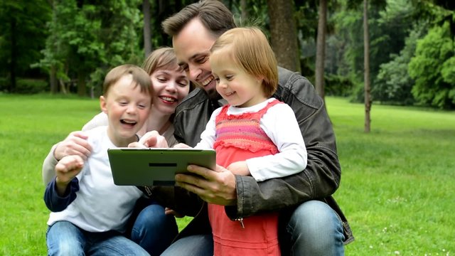 family (middle couple in love, cute girl and small boy) together work on tablet - park