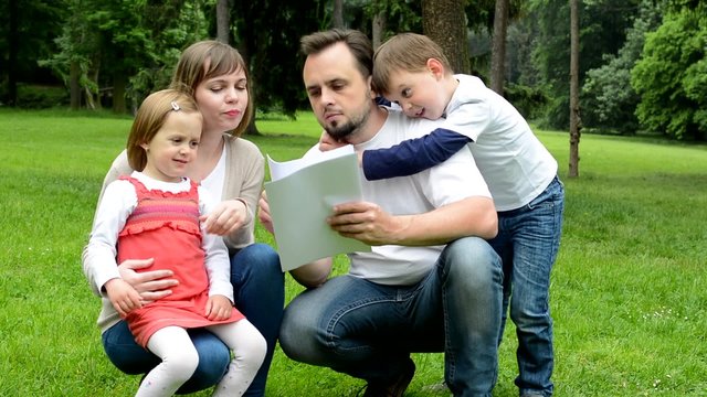 family (middle couple in love, cute girl and small boy) read document in the park