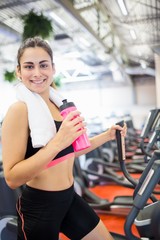 Fototapeta premium Smiling woman drinking on the cross trainer