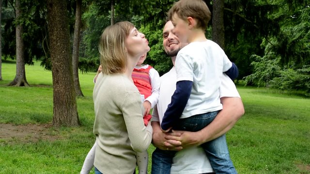 Family (middle couple in love, cute girl and small boy) give a kiss together in park