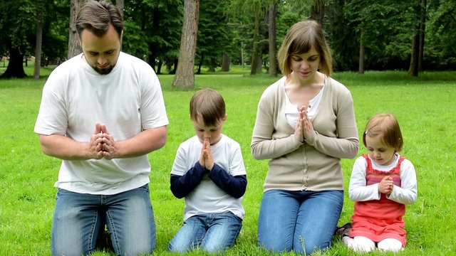 family (middle aged couple in love, boy and girl) pray in park (family kneeling on knees)