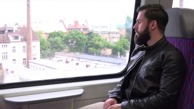 young handsome hipster man travel by train and looks out of the window - city
