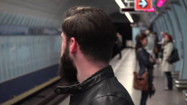 young handsome hipster man waits on metro in subway station - other people in background