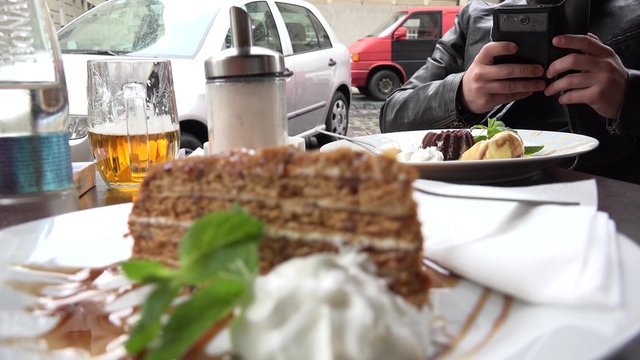 young handsome hipster man photographs food with smartphone (cake) - outdoor seating restaurant