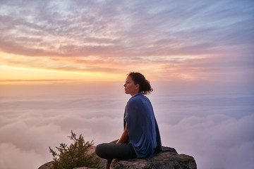 Woman sitting serenely on a mountain top in early morning