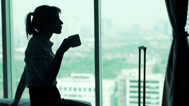 Young, pensive businesswoman drinking coffee by window in office