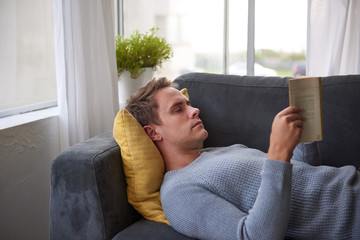 Young man reading comfortably on his couch at home