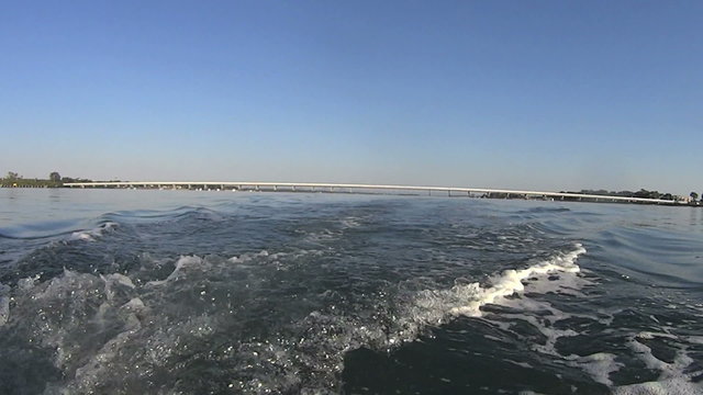 View from the stern of a dinghy with wake from outboard motor with bridge in background.