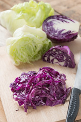 Chopped red cabbage and green lettuce on wooden cutting board.