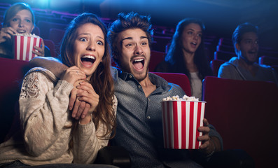 Young couple at the cinema watching an horror movie - obrazy, fototapety, plakaty