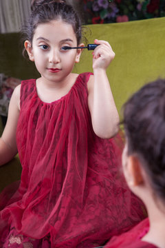 Small beautiful arab middle eastern girl with pretty red dress and lips doing makeup carefully at home in mirror. 8-10 years with dark brwon hairs and dark eyes.