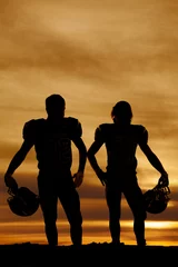 Fotobehang silhouette of football players holding helmets in the sunset © Poulsons Photography
