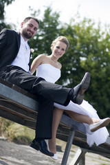 Bride and grom swinging their legs. Outdoors.