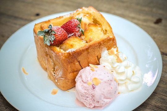 Selective focus of honey toast with fresh strawberry and icecream on wooden table - filter vintage style picture