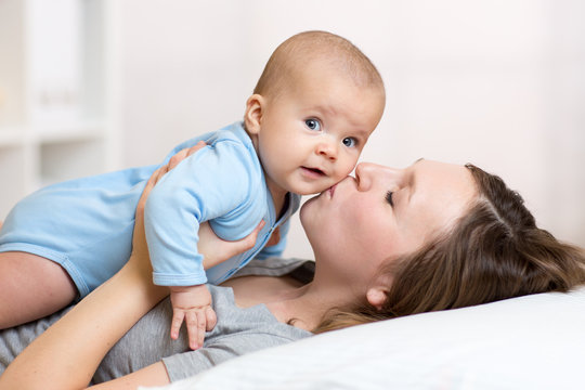 Mother kissing baby lying on bed in nursery