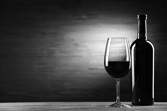 Wine bottle with glass on wooden background,  black and white retro stylization