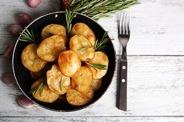 Delicious baked potato with rosemary in frying pan on table close up