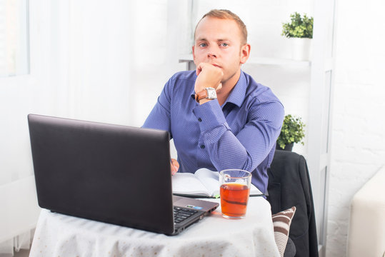 Businessman working in office, sitting at table with a laptop, looking camera.