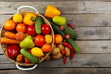 Heap of fresh fruits and vegetables in basket on wooden table close up
