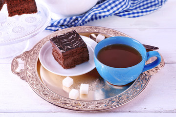 Served table with chocolate cake and a cup of tea on white wooden background