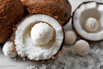 Candies in coconut flakes and fresh coconut on color wooden background