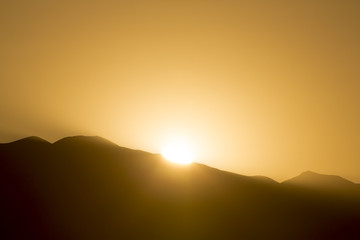 Dramatic sunset rays behind silhouette of of mountain