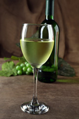 White wine glass against bottle and grape on wooden table