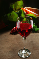 Red wine glass against wicker basket with grape and wine bottle on wooden table