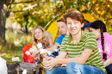 Friends hold marshmallow sitting on campsite