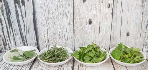 Fototapeta premium Basil leaves, rosemary. mint, parsley and sage leaves herbs in white bowl over wooden background