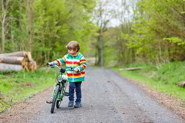Naklejka premium Little kid boy riding on a bike in forest