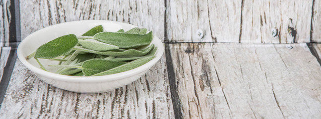 Obraz premium Sage leaves herb in white bowl over wooden background