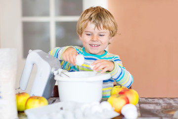 Funny blond kid boy baking apple cake indoors