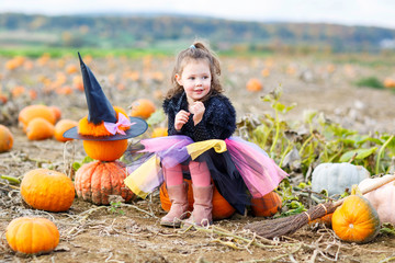 little girl wearing halloween witch costume on pumpkin patch