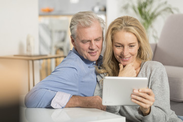 Mature couple sitting in sofa and using tablet pc