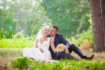 bride and groom sit on grass in the park