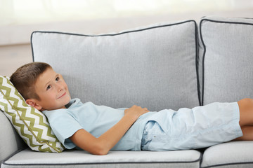 Little boy sitting on sofa, on home interior background