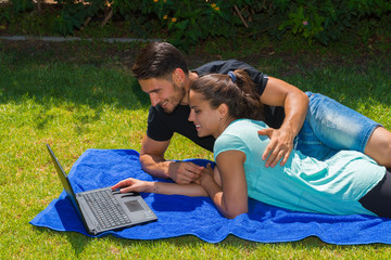 Young couple using a laptop lying on grass.