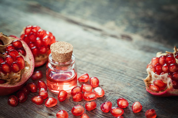 Pomegranate oil in bottle and garnet fruit with seeds on table.