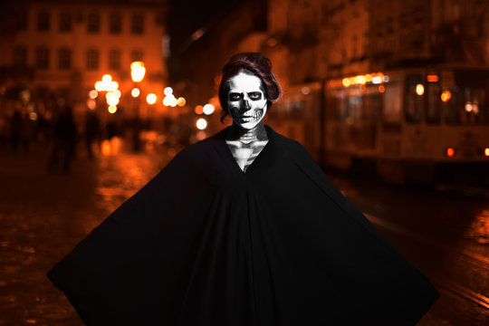 Young woman is standing on the street  in black costume with Halloween makeup . Street portrait