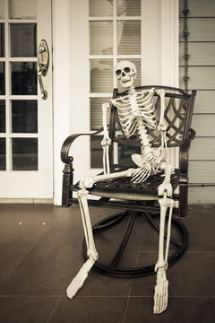 Skeleton ghost sit on a chair. Human skull waiting someone in Halloween day.