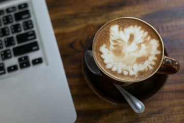 Hot latte coffee cup in cup on a table laptob in coffee shop.