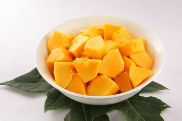 Bowl of fresh papaya fruit slices with papaya leaves.
