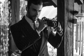 Black-white portrait of young beautiful fashionable man in classic suit with retro photo camera.
