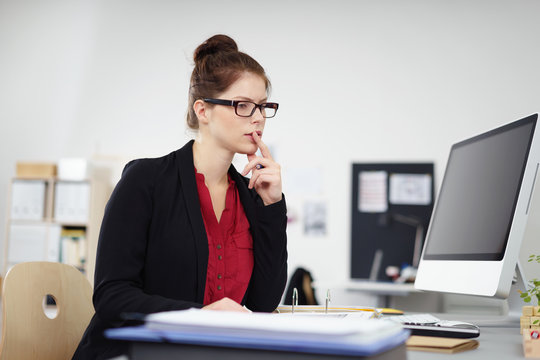 bürokauffrau sitzt am arbeitsplatz und denkt nach