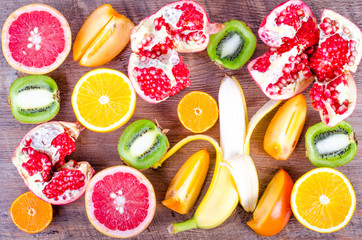 Fresh fruits on wooden background. Summer background. Raw and vegetarian eating background. Sliced orange, persimmon, kiwi, tangerine, banana, lemon, apple,  grapefruit, pomegranate, lime,  Top view