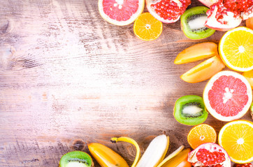 Fresh fruits on wooden background. Summer background. Raw and vegetarian eating frame. Sliced orange, persimmon, kiwi, tangerine, banana, lemon, apple,  grapefruit, pomegranate, lime,  Top view