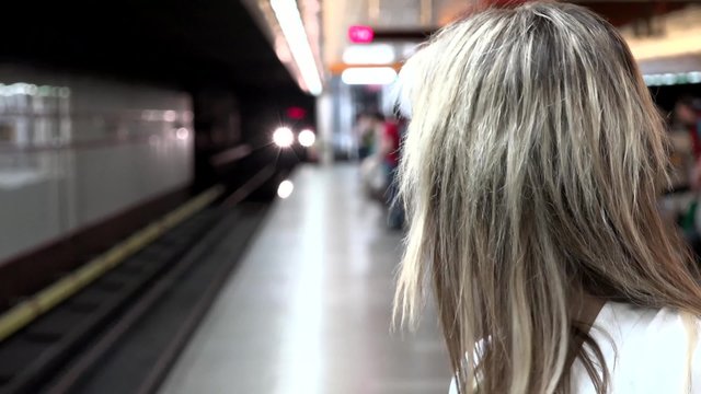 young attractive blonde woman waits for subway and looks around - arriving metro - other people in the background