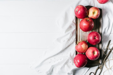 Red apples in a metal dish on white textiles and white wooden background top view