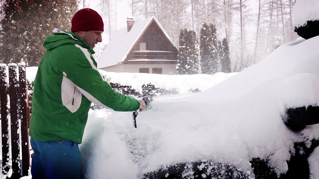 A man clears the snow off the car in the morning after a snowfall
